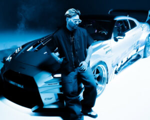 Wax Motif poses in front of a rally car